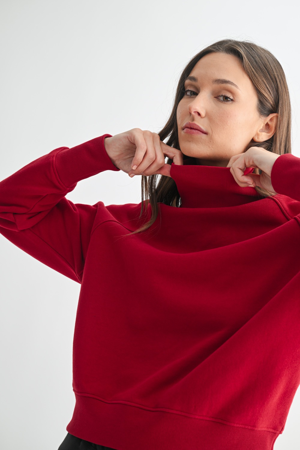 Model wearing a garnet red cotton raglan sleeve turtleneck sweater with ribbed trim and relaxed fit, styled for fall layering.