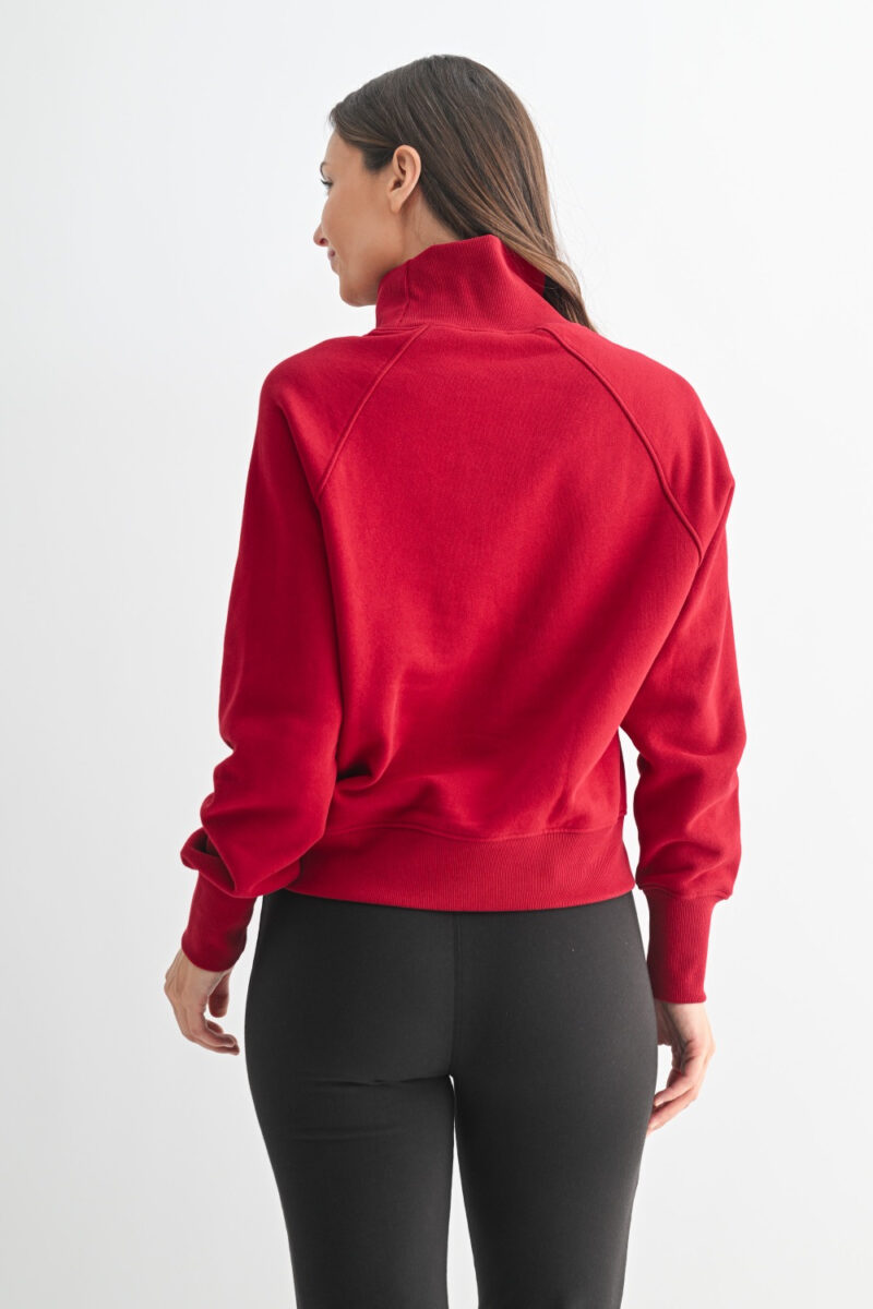 Model wearing a garnet red cotton raglan sleeve turtleneck sweater with ribbed trim and relaxed fit, styled for fall layering.